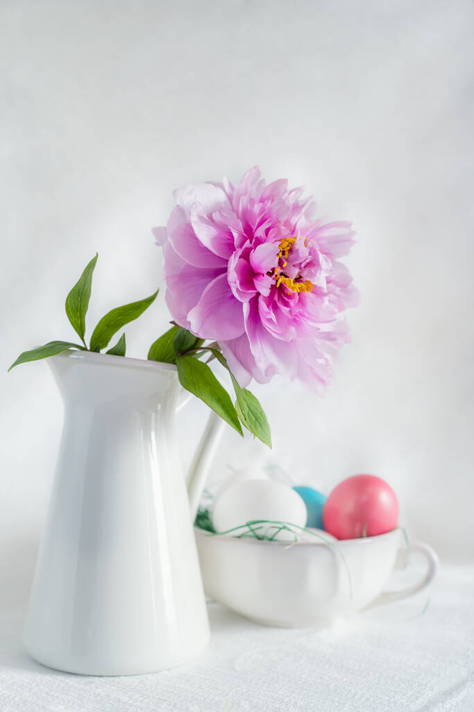 Easter still life with gorgeous pink peonies in a vase and an antique porcelain bowl with coloured eggs on a white background - Photo, Image