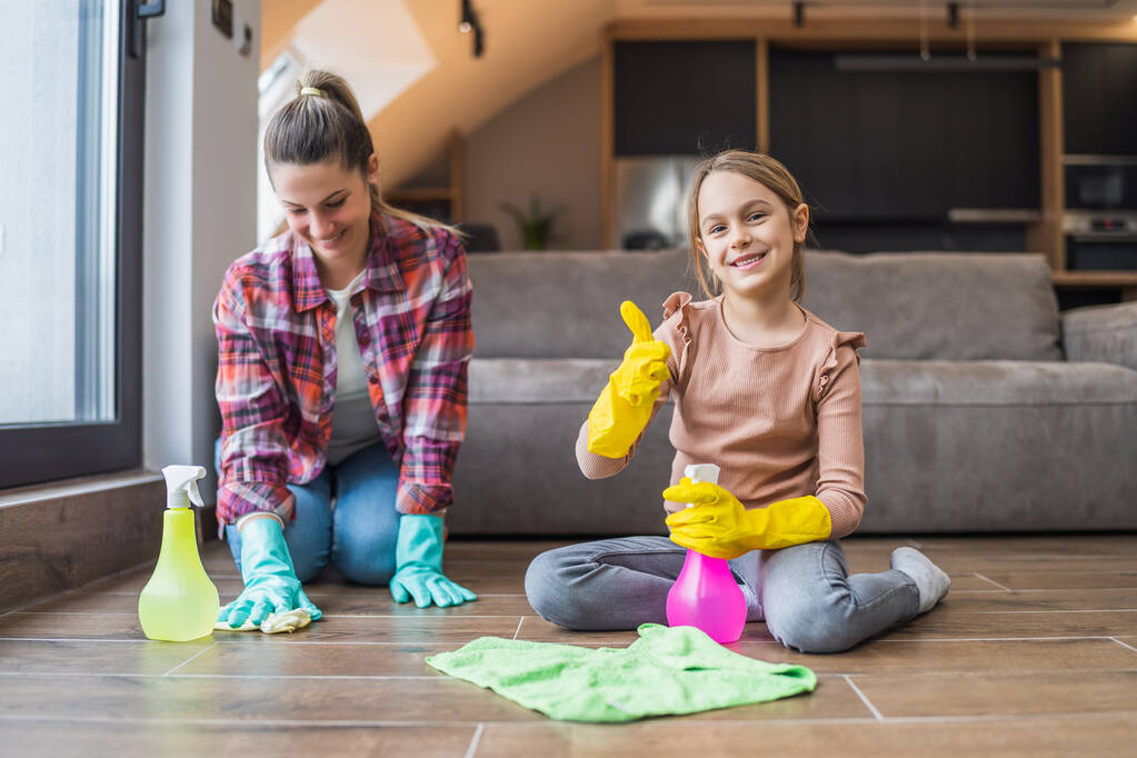 Feliz hija mostrando el pulgar hacia arriba mientras limpia la casa con su madre. - Foto, Imagen