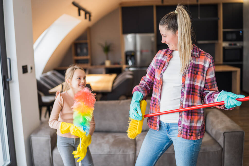 Ευτυχισμένη μητέρα και κόρη διασκεδάζουν ενώ καθαρίζουν το σπίτι μαζί.. - Φωτογραφία, εικόνα