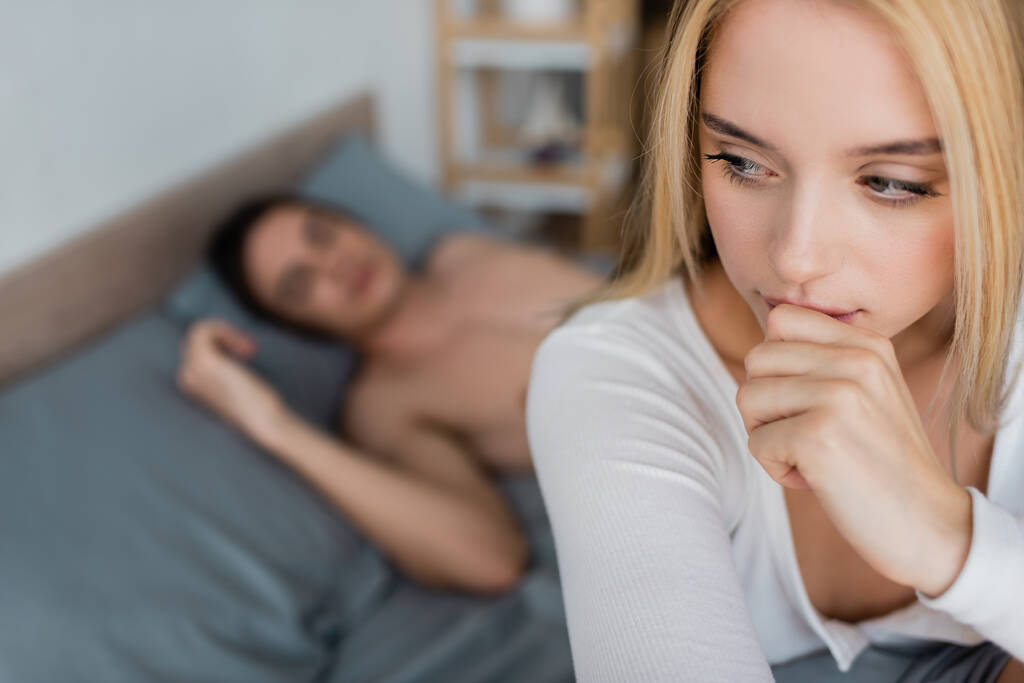 беспокойная женщина, прикрывающая рот, рядом с размытым мужчиной без рубашки, спящим после одной ночи  - Фото, изображение
