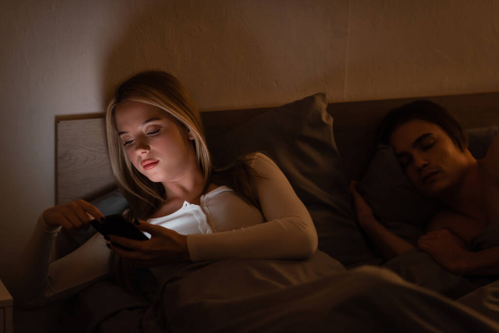 nevěrná žena pomocí smartphone vedle spícího přítele v noci, podvádění koncept   - Fotografie, Obrázek