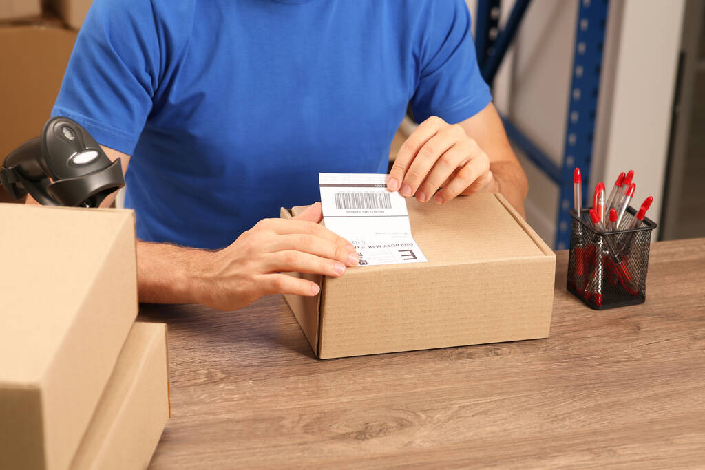 Trabajador de oficina de correos pegando código de barras en el paquete en el mostrador interior, primer plano - Foto, imagen