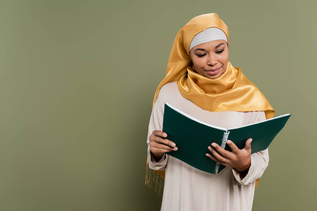 Πολυφυλετικός μουσουλμάνος φοιτητής κοιτάζοντας σημειωματάριο σε πράσινο φόντο - Φωτογραφία, εικόνα