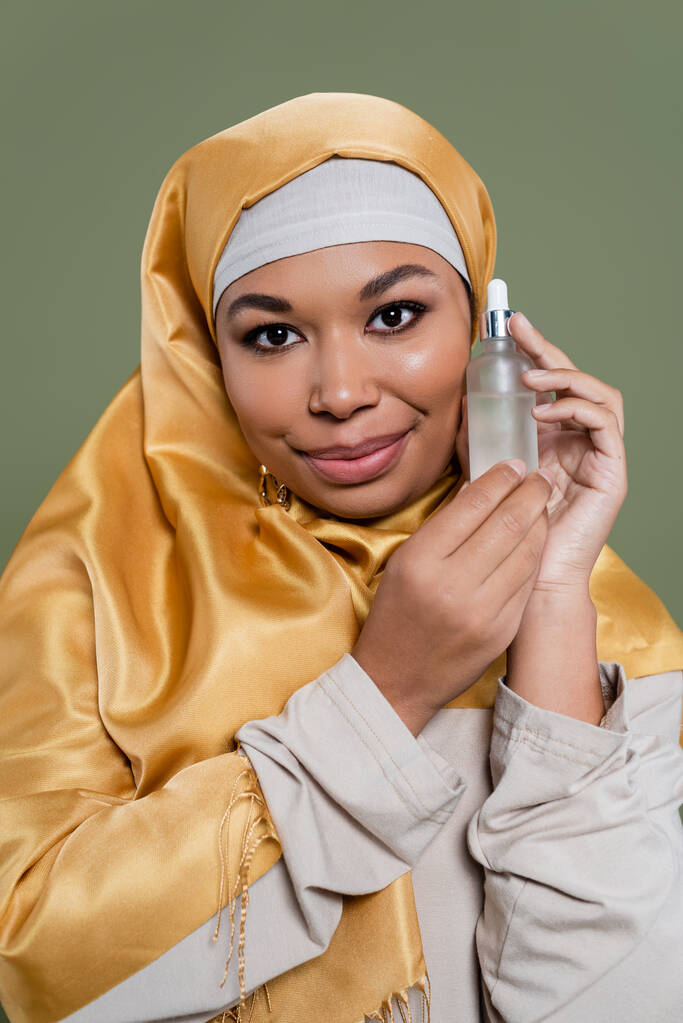 Πορτρέτο της πολυφυλετικής γυναίκας σε hijab εκμετάλλευση καλλυντικών ορού που απομονώνονται σε πράσινο  - Φωτογραφία, εικόνα