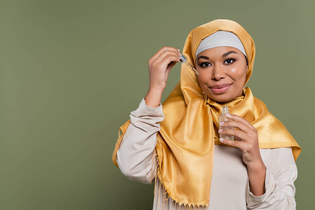 Nuori monirotuinen nainen hijabissa tilalla seerumi ja tiputin vihreällä taustalla - Valokuva, kuva