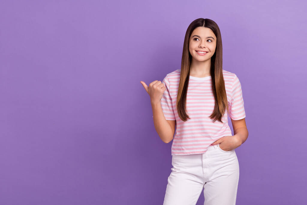 可愛いです思慮深い若い女の子の服を着てストライプ白ピンクtシャツ見て親指空のスペース孤立紫色の背景. - 写真・画像