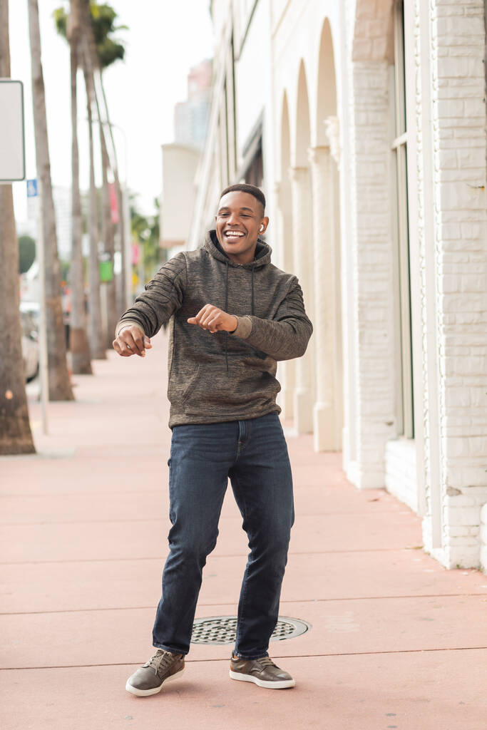hombre afroamericano feliz en auriculares inalámbricos que se divierten en la calle en Miami  - Foto, imagen