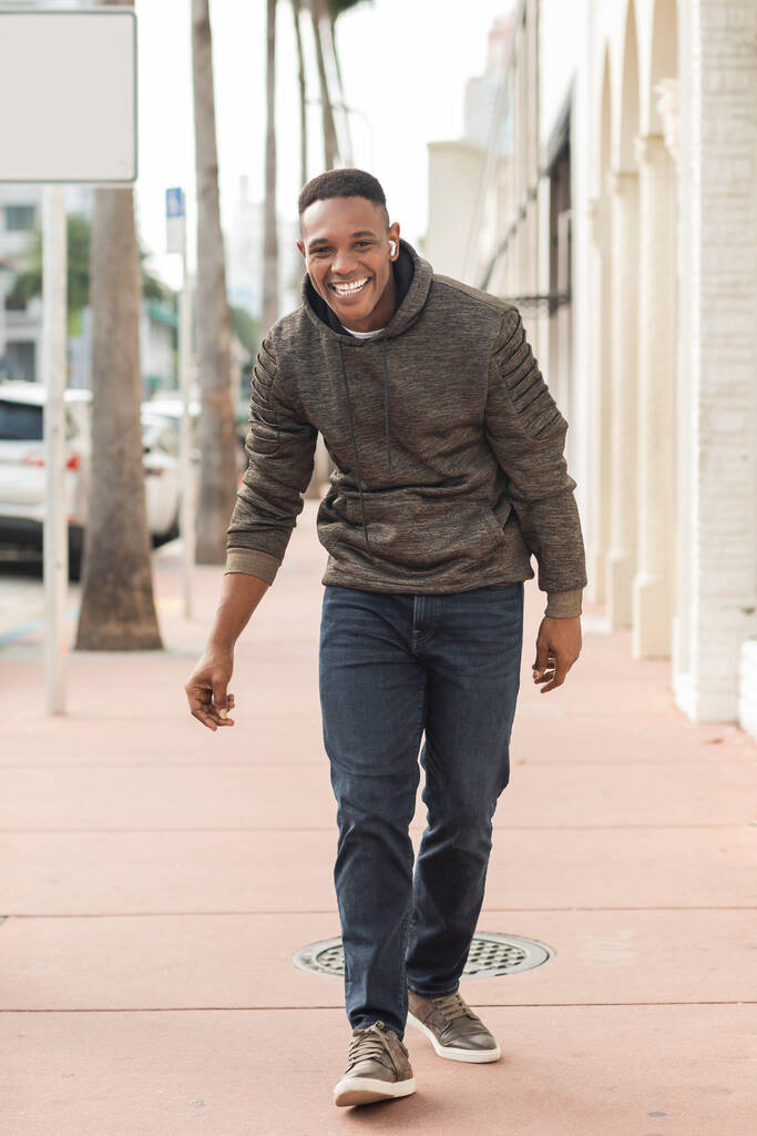 nadšený africký Američan v bezdrátových sluchátkách chůze na ulici v Miami  - Fotografie, Obrázek