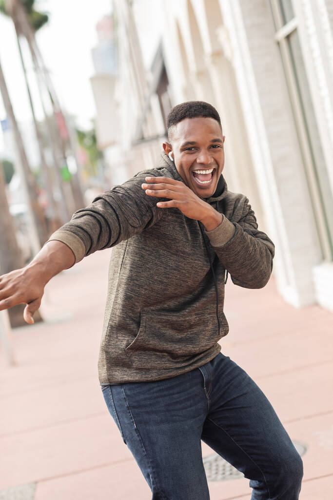 возбужденный африканский американец в беспроводных наушниках слушает музыку и танцует на улице в Майами  - Фото, изображение