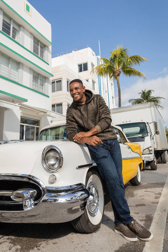 MIAMI, FLORIDA, USA - 15 DICEMBRE 2022: felice uomo afroamericano in piedi vicino a un'auto d'epoca  - Foto, immagini