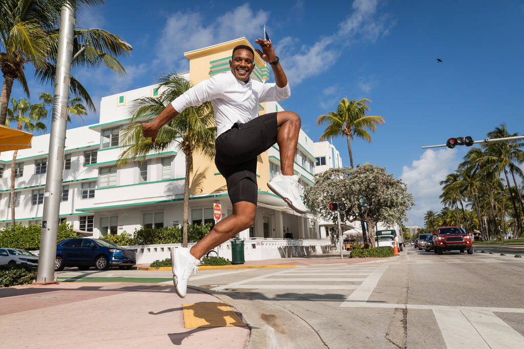 allegro uomo afroamericano che salta accanto alle palme e al moderno condominio a Miami  - Foto, immagini