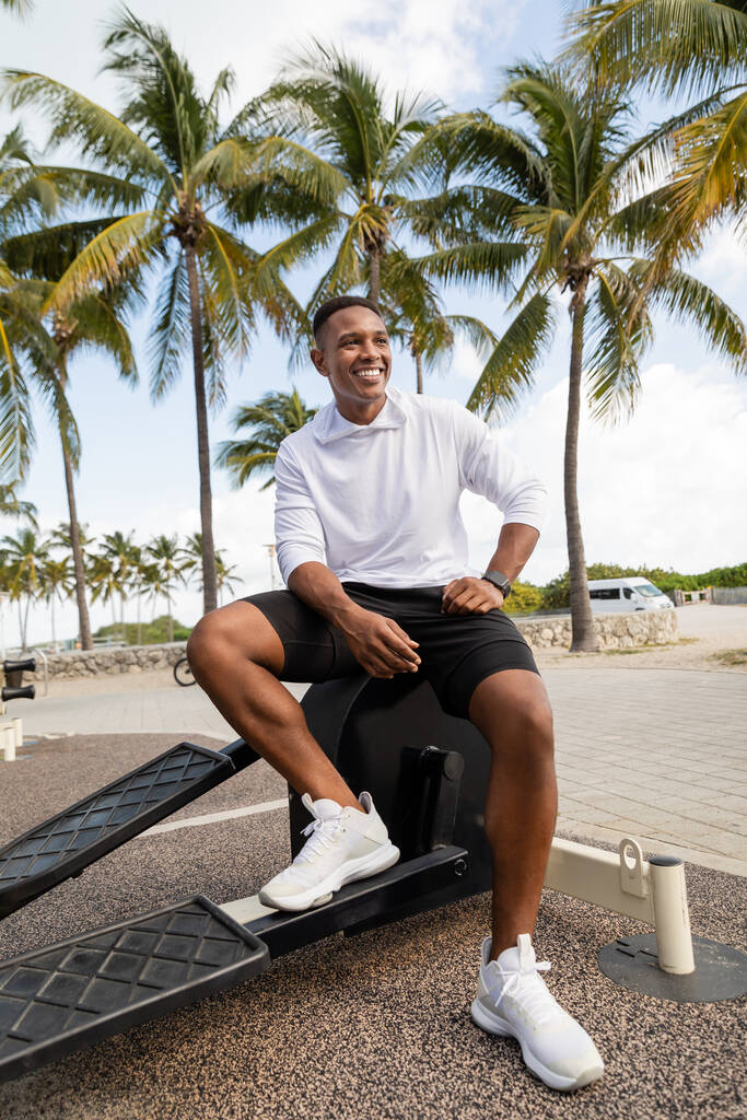 безтурботний афроамериканський спортсмен, що сидить на тренувальному обладнанні у відкритому тренажерному залі у Маямі - Фото, зображення