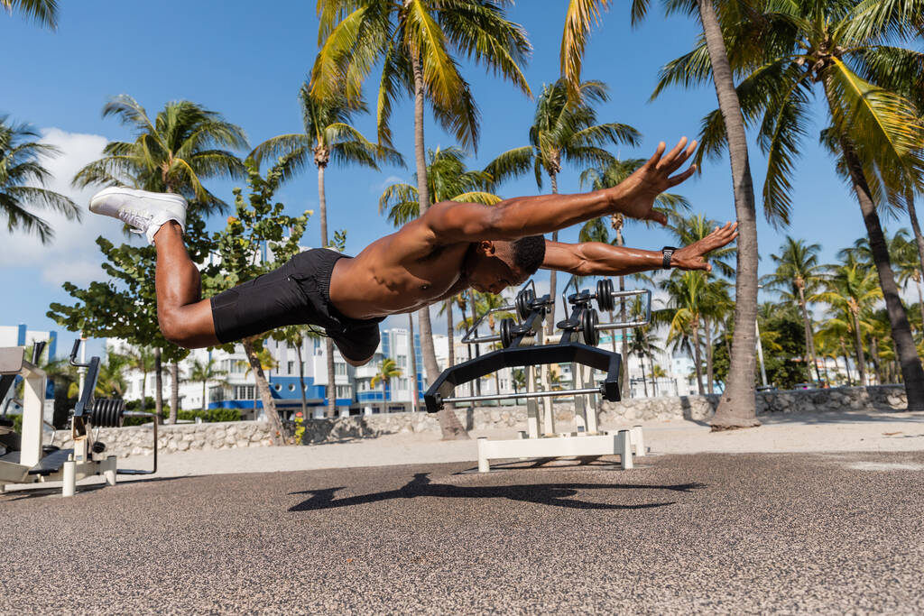 ημίγυμνος Αφροαμερικάνος αθλητής που πέφτει στο έδαφος δίπλα σε φοίνικες στην παραλία του Μαϊάμι  - Φωτογραφία, εικόνα