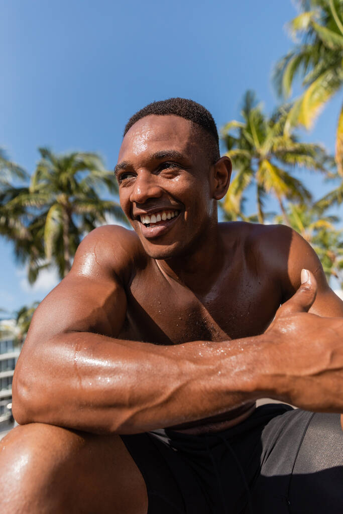 retrato de desportista afro-americano suado e feliz sem camisa olhando para longe após o treino  - Foto, Imagem