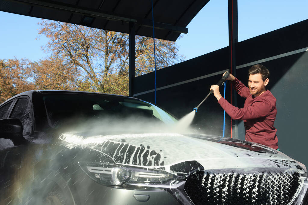Worker washing auto with high pressure water jet at outdoor car wash - Foto, Imagem
