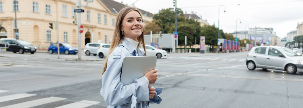 gelukkige vrouw in blauwe trench jas met laptop en kruising weg op straat in Wenen, banner  - Foto, afbeelding