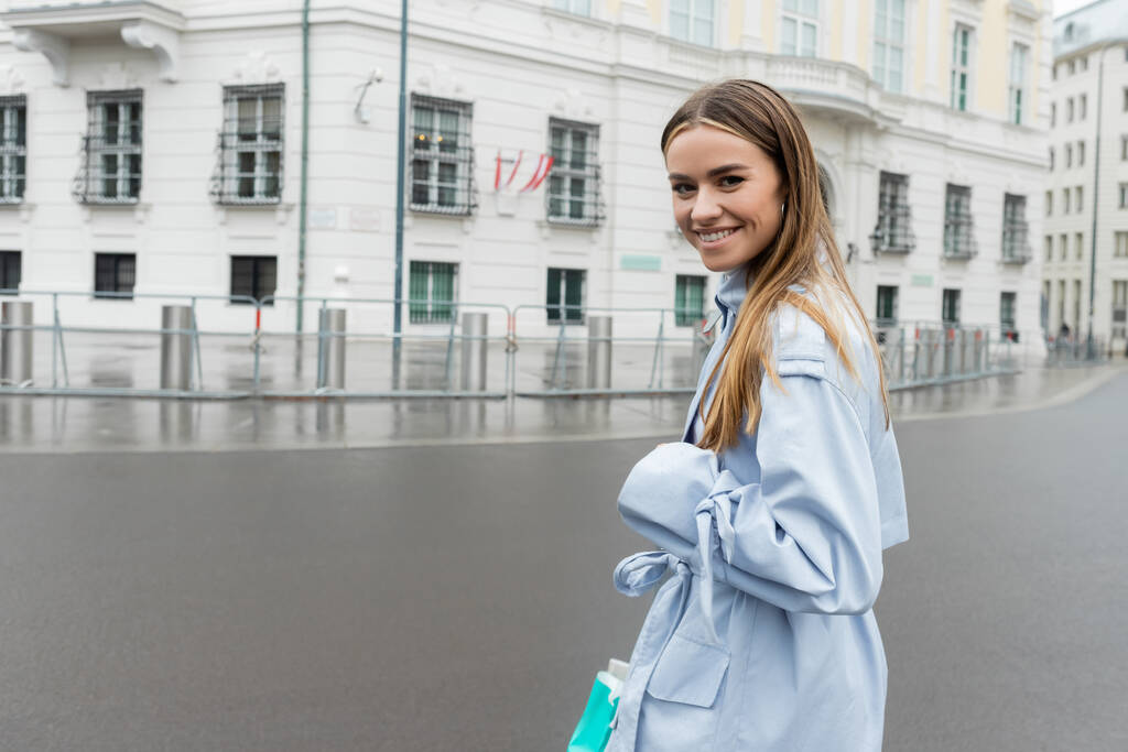 Zufriedene Frau im blauen Trenchcoat lächelt auf Wiener Straße  - Foto, Bild