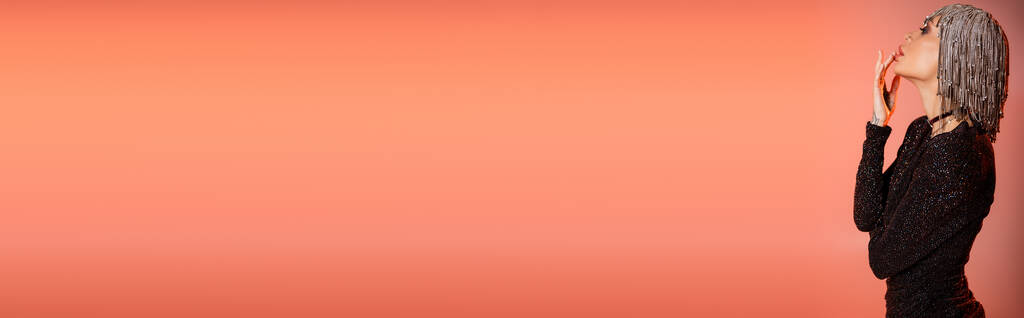 вид збоку гламурної жінки в металевій головній убірці і чорна сукня люрекса, що торкається губ на кораловому рожевому фоні, банер
 - Фото, зображення