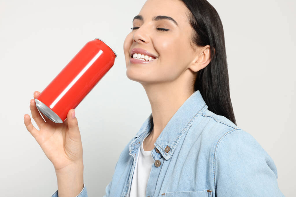 Όμορφη ευτυχισμένη γυναίκα πίνοντας από το κόκκινο αναψυκτικό μπορεί σε ανοιχτό γκρι φόντο - Φωτογραφία, εικόνα