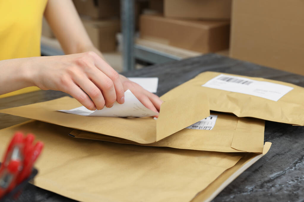 Почтальон приклеивает штрих-код на посылку у прилавка в помещении, крупным планом - Фото, изображение