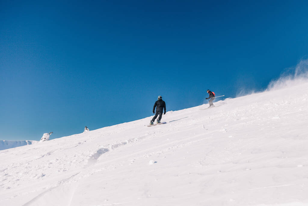 Karpaty, Ukrajina, 8. února2023. Lyžaři a snowboardisté freeride za jasného slunečného počasí na svazích hor u letoviska Dragobrat. Kvalitní fotografie - Fotografie, Obrázek