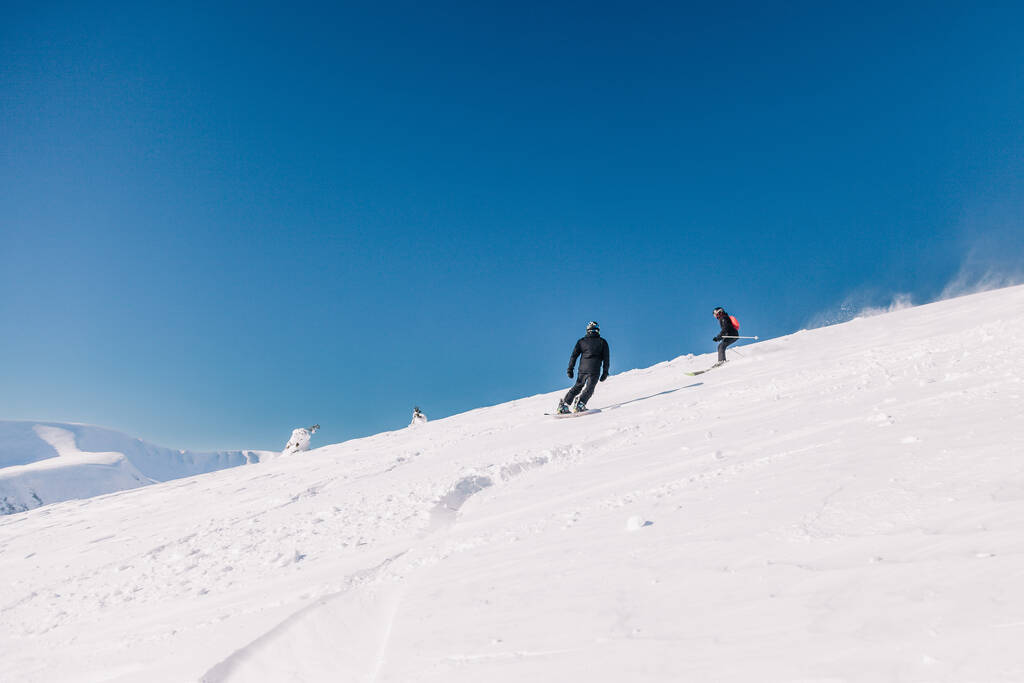 Karpaty, Ukraine, February 8, 2023. Skiers and snowboarders freeride in clear sunny weather on the slopes of the mountains near the resort of Dragobrat. High quality photo - Φωτογραφία, εικόνα