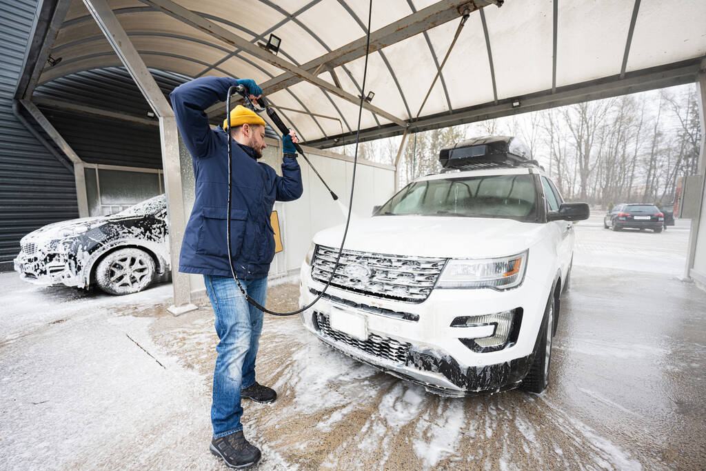 Man washing high pressure water american SUV car with roof rack at self service wash in cold weather. - Foto, Bild