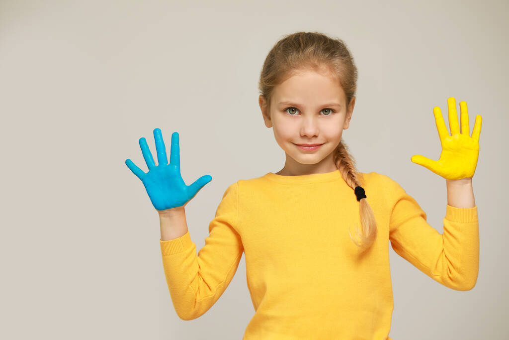 Little girl with hands painted in Ukrainian flag colors on light grey background, space for text. Love Ukraine concept - Photo, Image