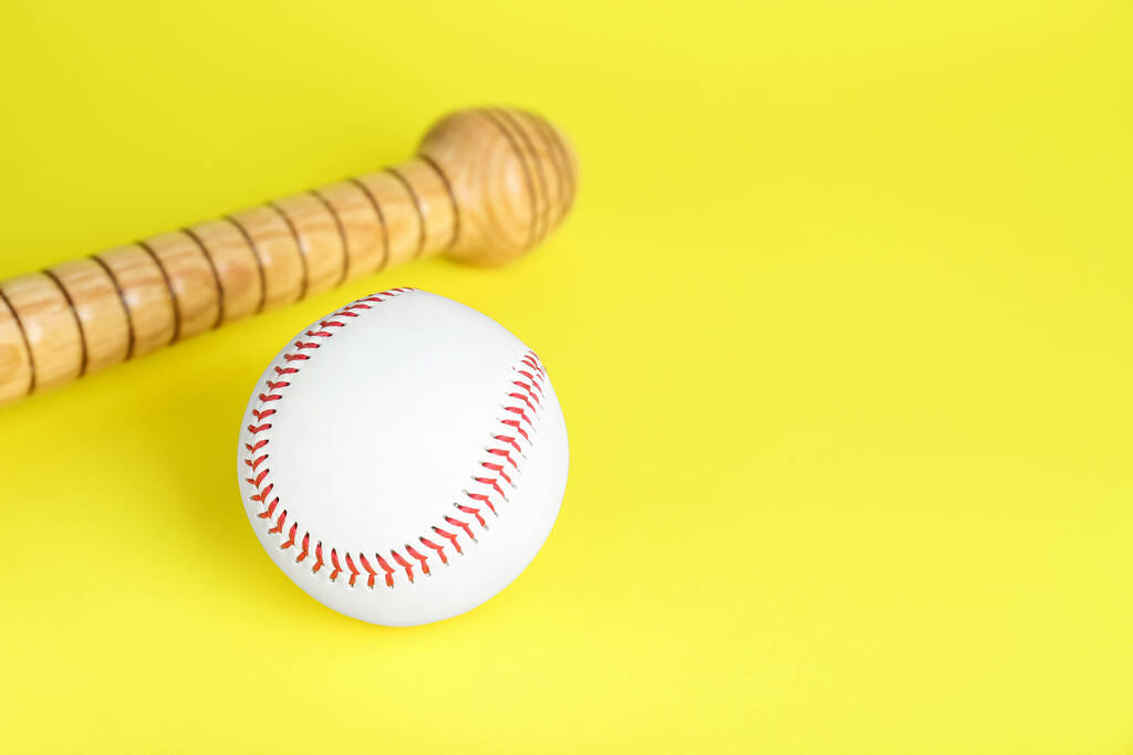 Drewniany kij baseballowy i piłka na żółtym tle, miejsce na tekst. Sprzęt sportowy - Zdjęcie, obraz