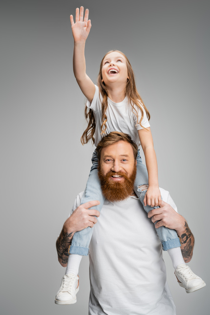 Весела дитина піднімає руку, сидячи на плечах батька ізольовано на сірому
  - Фото, зображення