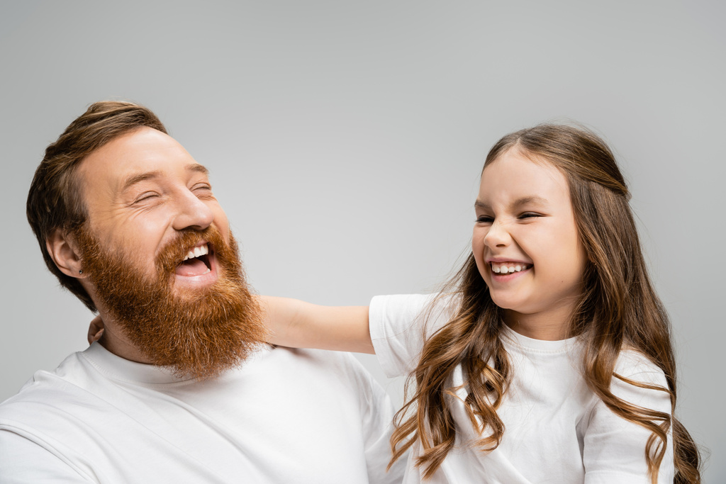 Ενθουσιασμένο παιδί και πατέρας με λευκά μπλουζάκια γελώντας απομονωμένοι στο γκρι  - Φωτογραφία, εικόνα