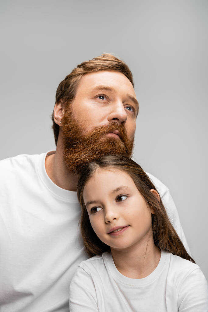 Retrato de hombre e hija barbudos en camisetas blancas mirando hacia otro lado aislados en gris   - Foto, imagen