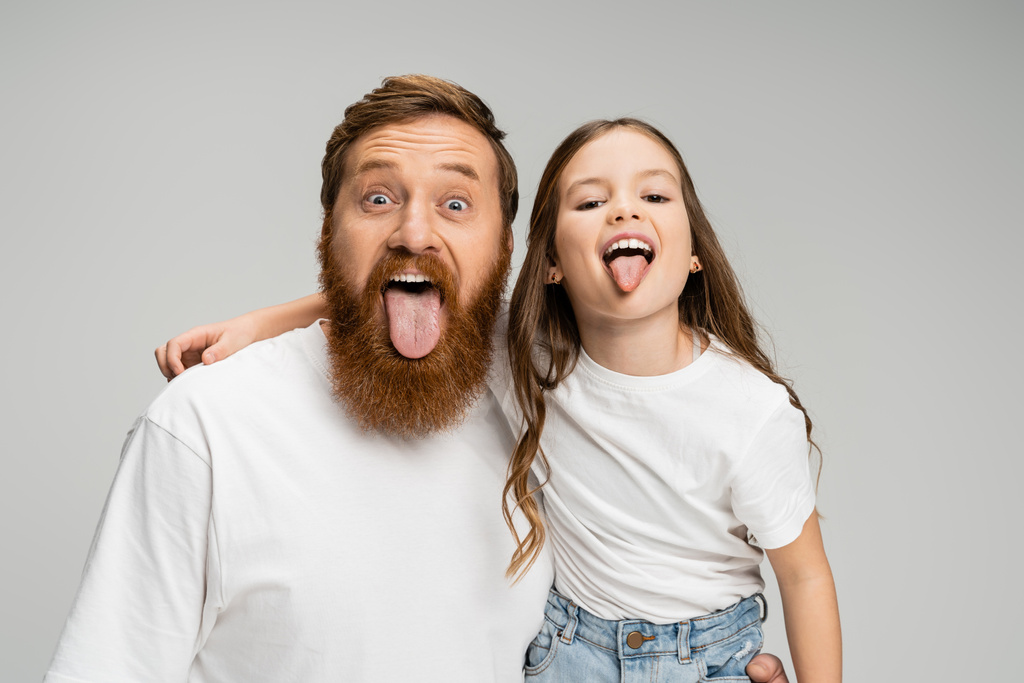 Preteen kid and bearded dad sticking out tongues isolated on grey   - Photo, Image