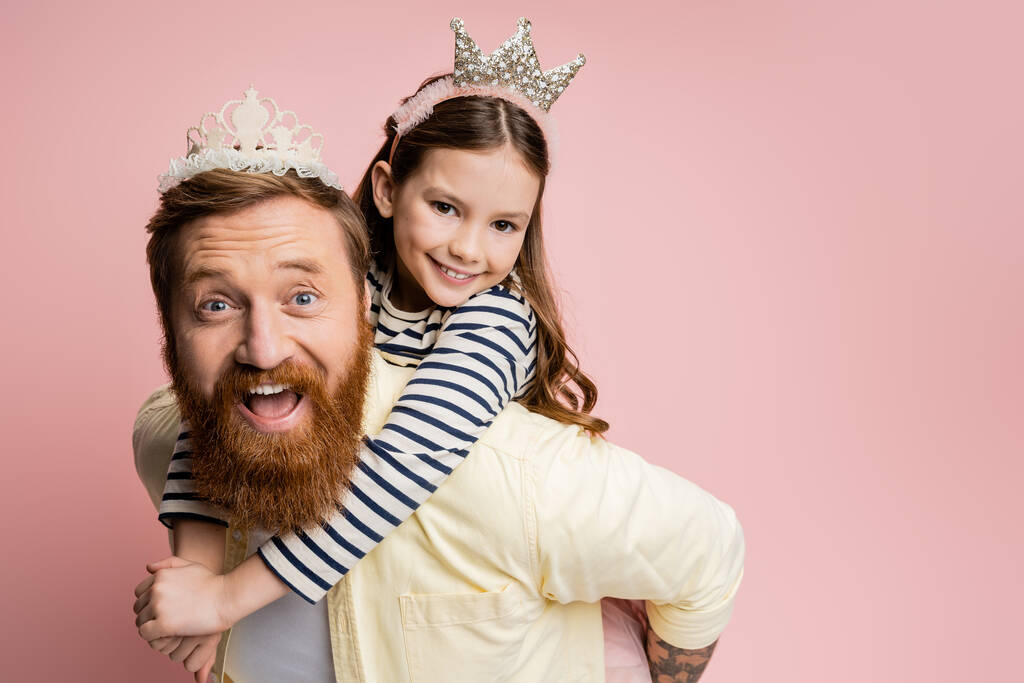 Sonriente niña abrazando padre con diadema de corona aislado en rosa   - Foto, imagen