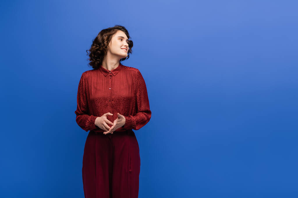cheerful language teacher in maroon color outfit smiling while looking away isolated on blue  - Photo, Image