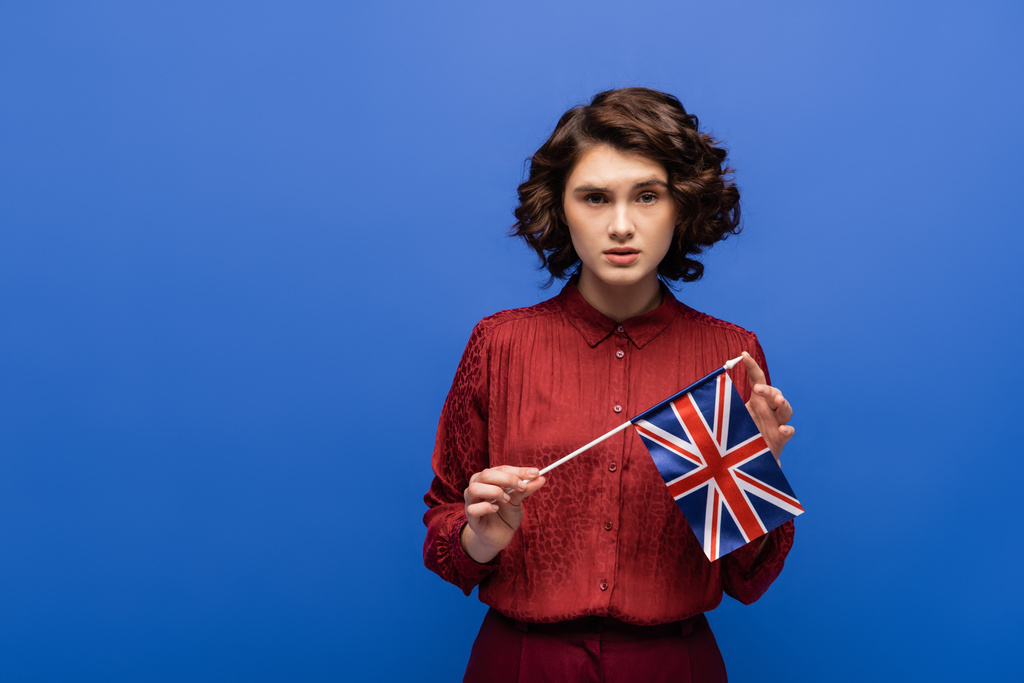 σοβαρός καθηγητής γλώσσας με σημαία Ηνωμένου Βασιλείου, απομονωμένος σε μπλε χρώμα  - Φωτογραφία, εικόνα