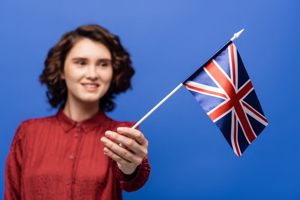 estudante alegre com cabelo encaracolado olhando para a bandeira do Reino Unido isolado em azul  - Foto, Imagem