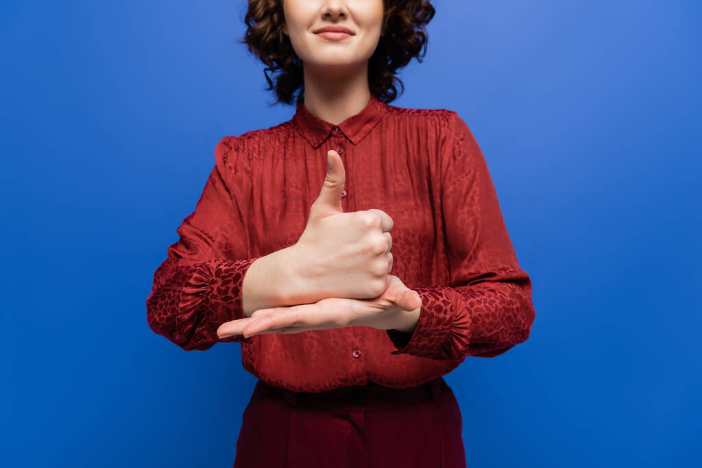 Burgundy bluz giyen pozitif kadının kısmi görüntüsü mavi üzerine izole edilmiş işaret dili üzerinde yardım anlamına geliyor. - Fotoğraf, Görsel