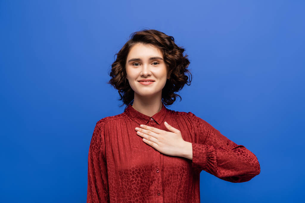 cheerful woman looking at camera and telling please on sign language isolated on blue - Photo, Image