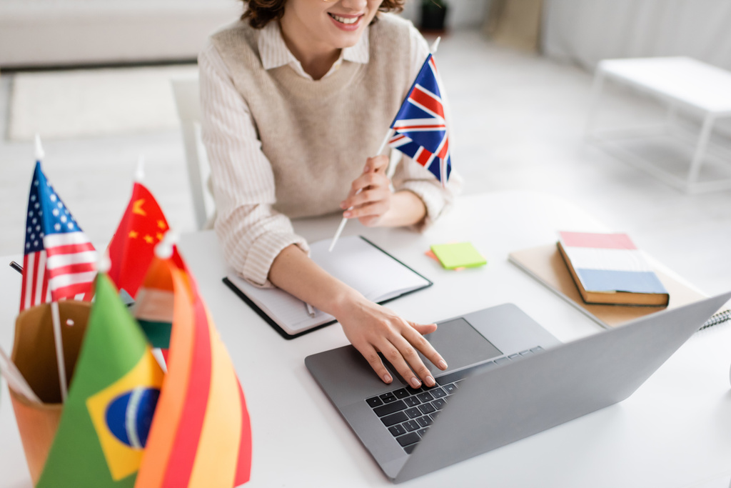 bijgesneden weergave van lachende taaldocent met vlag van Verenigd Koninkrijk met laptop tijdens online les thuis - Foto, afbeelding