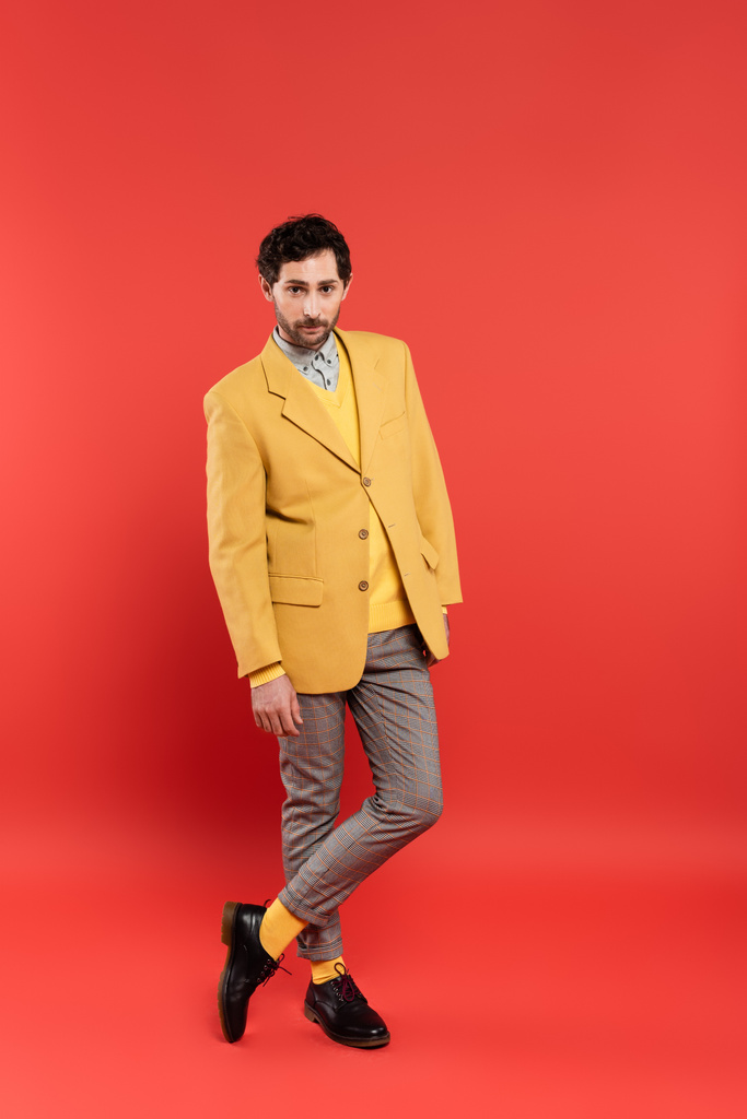 Comprimento total do homem na moda em calças xadrez e jaqueta em pé no fundo vermelho - Foto, Imagem