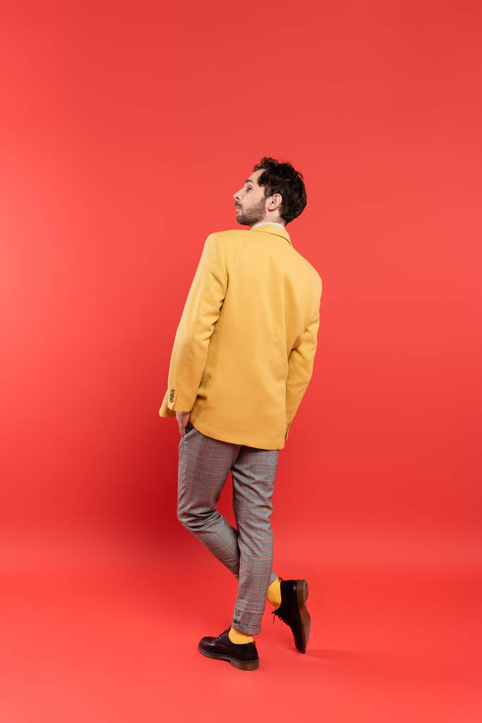 Вид сбоку стильный мужчина в желтой куртке позирует на кораллово-красном фоне - Фото, изображение