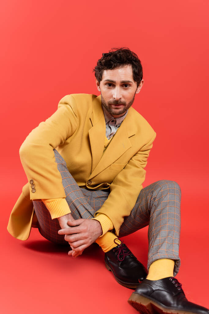 Hombre de moda y morena en chaqueta amarilla sentado sobre fondo rojo coral - Foto, imagen