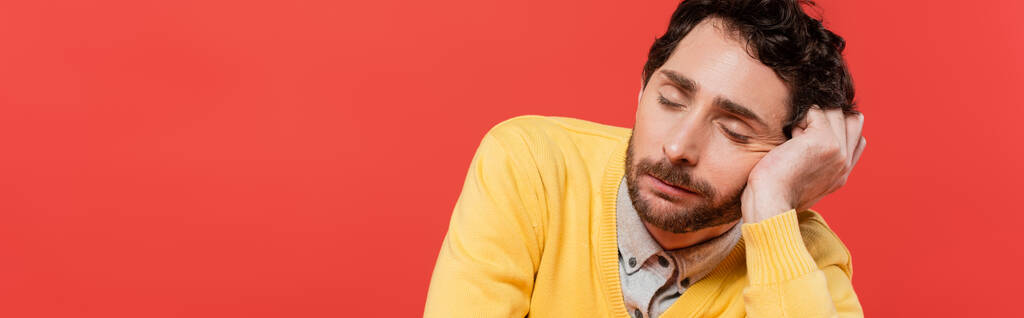 zmęczony mężczyzna w żółtym swetrze z długim rękawem śpiący na koralowym tle, sztandar  - Zdjęcie, obraz