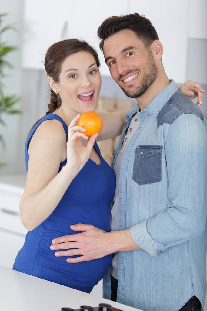 retrato del marido abrazando esposa embarazada con naranja fresca - Foto, imagen