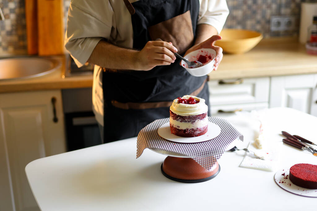 En esta foto, podemos ver a un chef de pastelería trabajando en la creación de un magnífico pastel. Sus manos manipulan hábilmente los ingredientes, dándoles lo necesario - Foto, imagen
