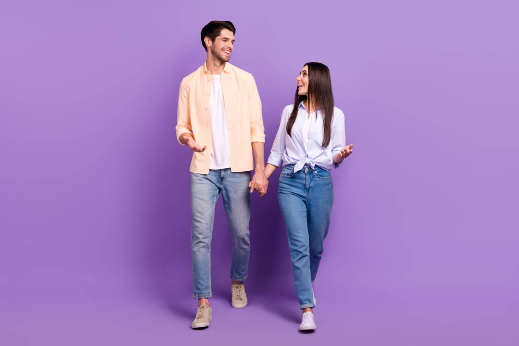 Plná délka portrét dvou idylických pozitivních lidí držet ruce chůze chatování mluvit izolované na fialové barvy pozadí. - Fotografie, Obrázek