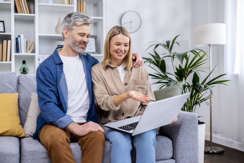 Ältere ältere Paar Mann und Frau sitzen zu Hause im Wohnzimmer auf dem Sofa, Menschen in der Liebe mit Laptop, haben Spaß bei der Auswahl von Produkten in Online-Internet-Shop zusammen. - Foto, Bild