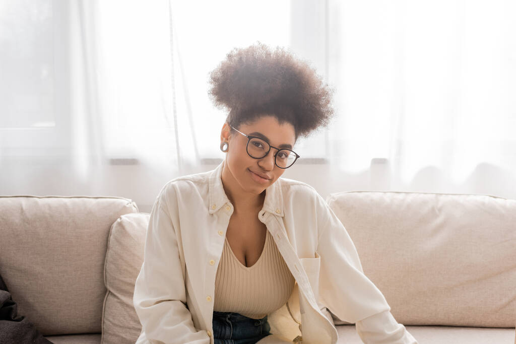 Femme afro-américaine insouciante avec des lunettes regardant la caméra à la maison  - Photo, image