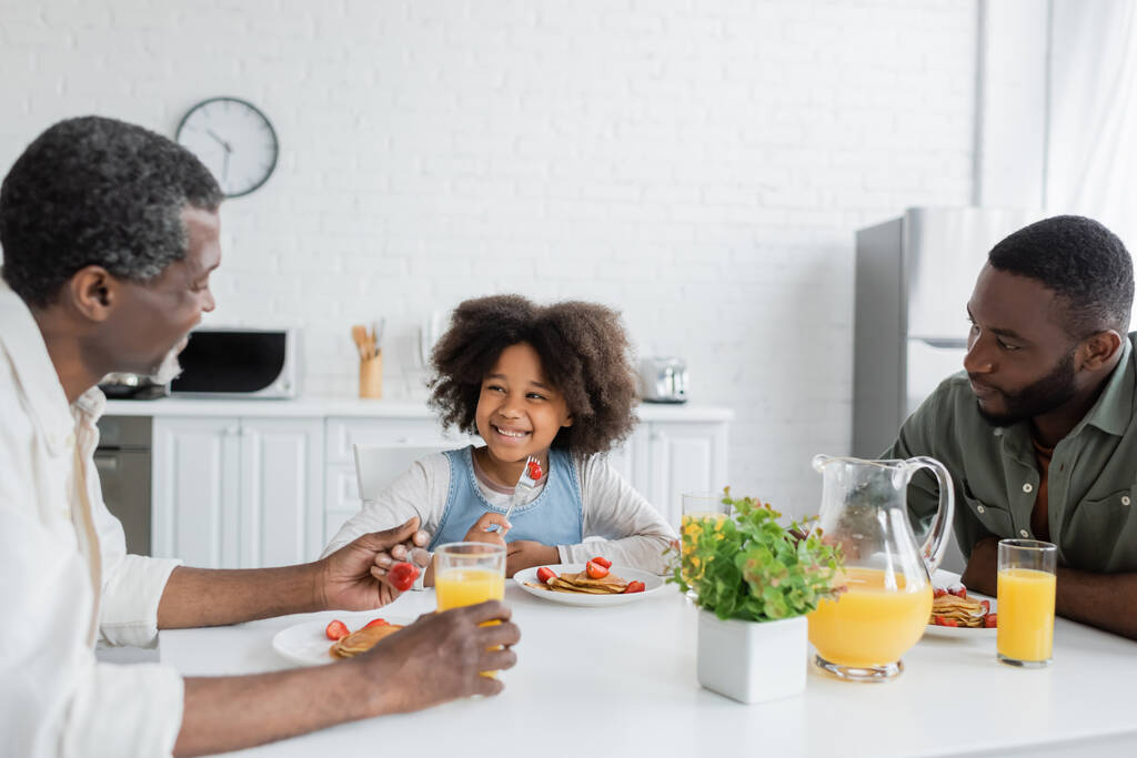 счастливый африканский американец смотрит на дедушку во время семейного завтрака  - Фото, изображение